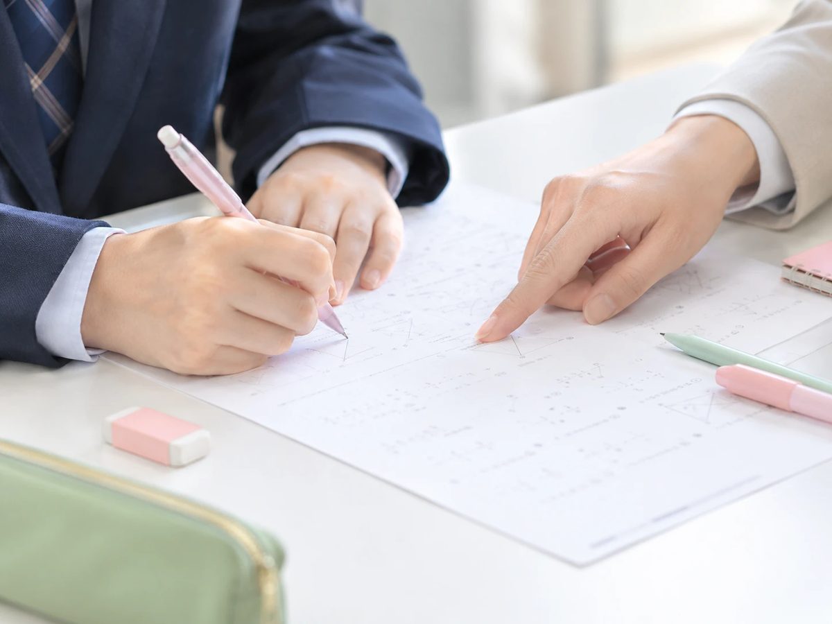 プリントに取り組む生徒の手元と、問題を指さす先生の手
